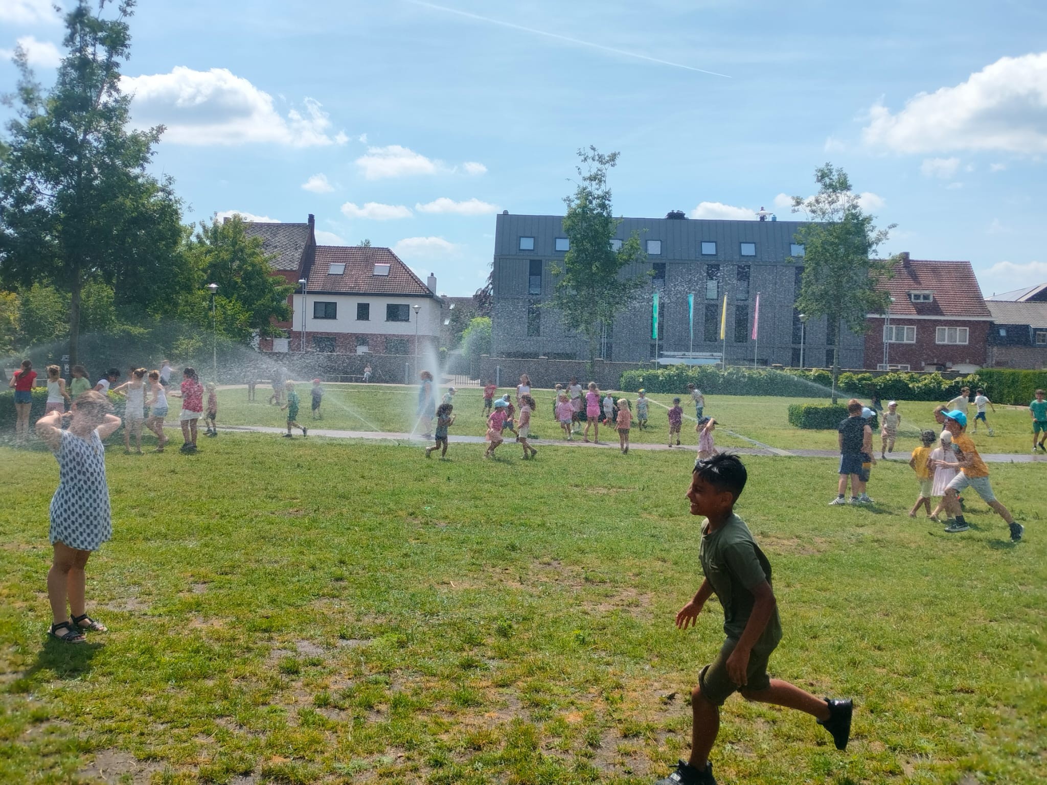 Kinderen spelen in het gras onder de sproeiers 